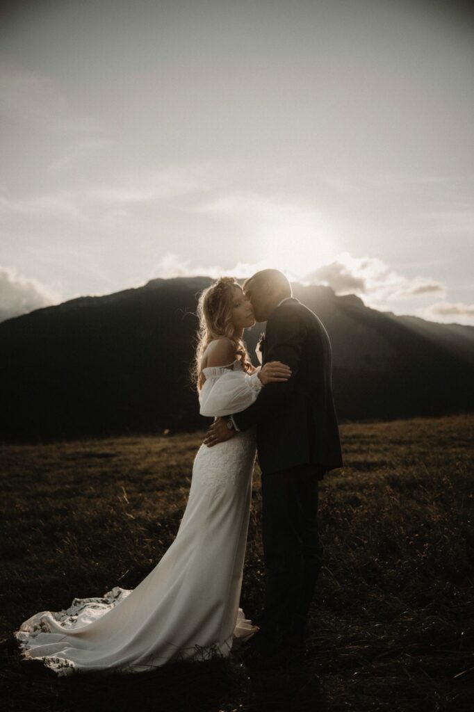 photographie d'un couple de marié dans le massif du vercors au coucher du soleil. Le couple s'embrasse alors que le soleil passe tout juste derrière la montagne créant ainsi une ambiance chaleureuse de photo de mariage